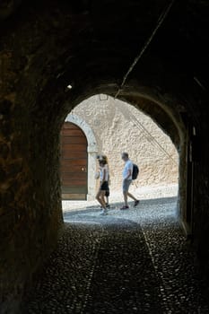 Tourists exploring the old town in the narrow streets of Malcesine on Lake Garda in Italy seen through a tunnel