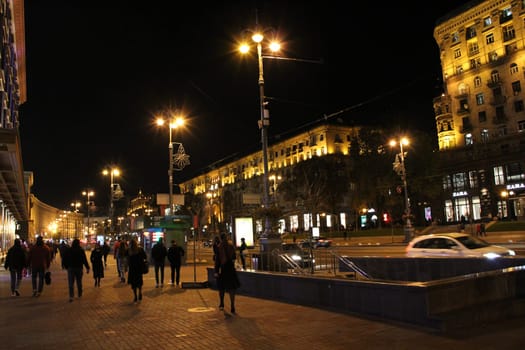 People walk along evening street in central part of Kyiv. People walk on street Khreshchatyk. Main street of Ukraine in evening. Illuminated street of evening city