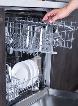 Housework open dishwasher and man putting a glass in the machine. High quality photo