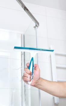 hand with glass scraper cleans glass in shower. High quality photo