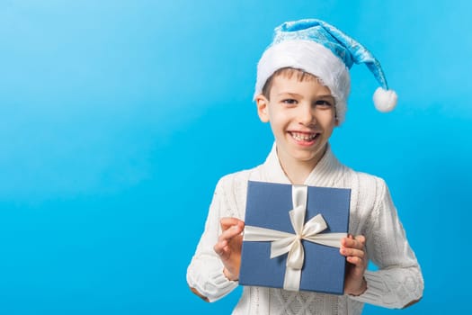 Happy little boy in blue Christmas hat with a gift box copy space. Empty place for your text. Winter holidays and present concept