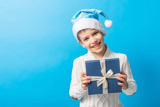 Happy little boy in blue Christmas hat with a gift box copy space. Empty place for your text. Winter holidays and present concept
