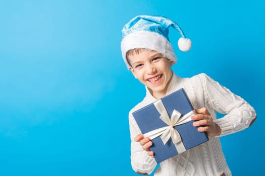 Happy little boy in blue Christmas hat with a gift box copy space. Empty place for your text. Winter holidays and present concept