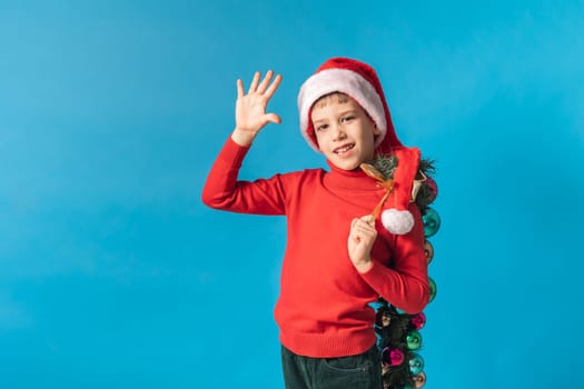 Cheerful child in santa hat hold christmas decorative balls on blue background, Xmas and holidays concept mockup. Generation alpha and gen alpha children