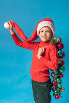 Cheerful child in santa hat hold christmas decorative balls on blue background, Xmas and holidays concept mockup. Generation alpha and gen alpha children