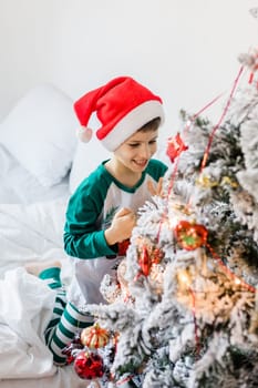 Close up of caucasian child hands putting ornaments on Christmas tree style in gold and white color