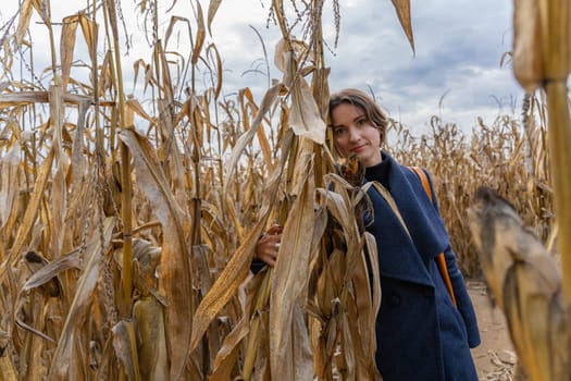 Woman standing in autumn in cornfield and looking at camera.