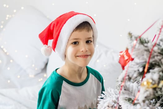 Child decorates Christmas tree. The boy is holding a Christmas toy. Morning before christmas at home. Generation alpha and gen alpha children