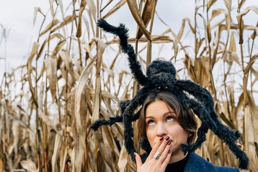 A woman covers her mouth with her hand in fear because of a toy large spider on her head. Halloween costumes and decorations.