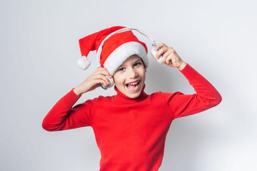 Funny child boy holds listening to Christmas music with Santa Claus hat on white background. Generation alpha and gen alpha children