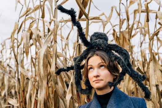Huge shaggy black toy spider on the head of a woman in a cornfield. Halloween decor concept.