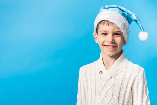 Exited child in blue Santa hat waiting Christmas time or presents on blue background with copy space. Mockup. Generation alpha and gen alpha.