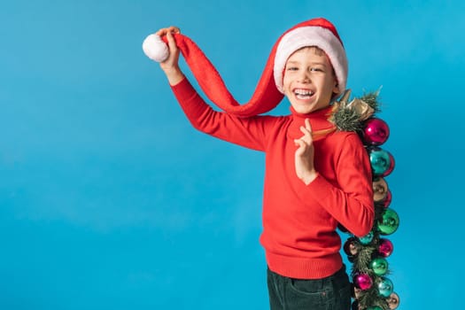 Cheerful child in santa hat hold christmas decorative balls on blue background, Xmas and holidays concept mockup. Generation alpha and gen alpha children