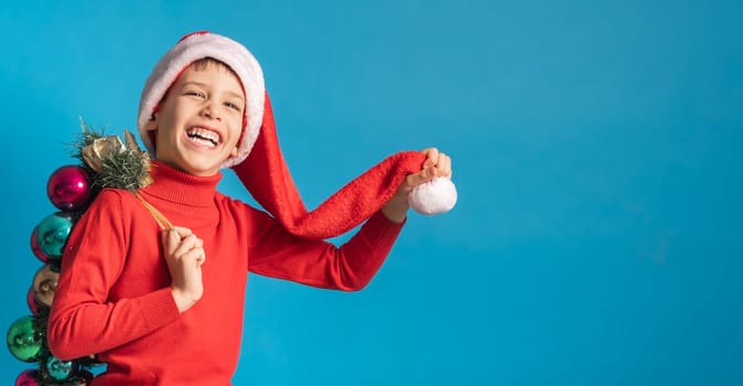Cheerful child in santa hat hold christmas decorative balls on blue background, Xmas and holidays concept mockup. Generation alpha and gen alpha children