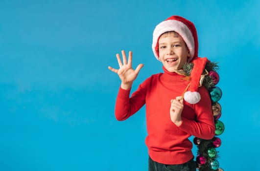 Cheerful child in santa hat hold christmas decorative balls on blue background, Xmas and holidays concept mockup. Generation alpha and gen alpha children