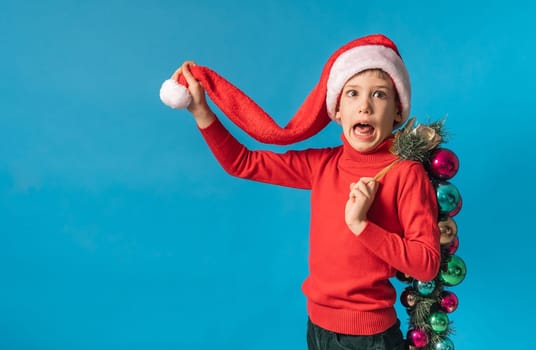 Cheerful child in santa hat hold christmas decorative balls on blue background, Xmas and holidays concept mockup. Generation alpha and gen alpha children