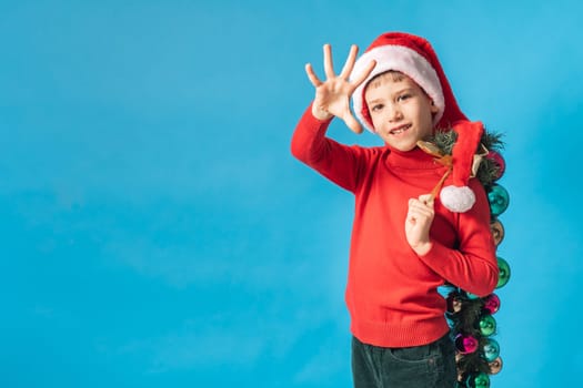 Cheerful child in santa hat hold christmas decorative balls on blue background, Xmas and holidays concept mockup. Generation alpha and gen alpha children