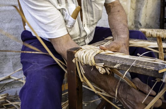Detail of older man working dry wicker with his hands, crafts