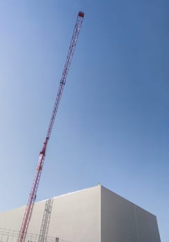 Worker on the top of a building under construction with red crane. Blue cloudy sky at background