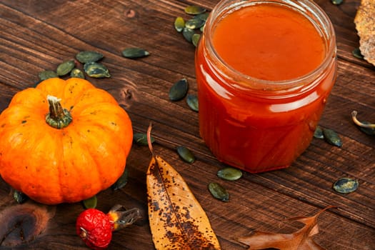 Pumpkin jam in a glass jar and fresh pumpkins on old wooden table.