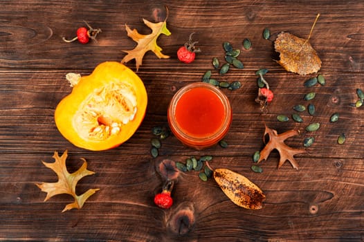 Pumpkin jam in a glass jar and fresh pumpkins on old wooden table.