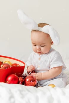 Christmas Baby in Santa Hat Child playing with baubles. Present Gift Box over Holiday Lights background and Merry Christmas