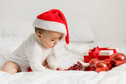 Christmas Baby in Santa Hat, Child holding christmas bauble near Present Gift Box over Holiday Lights