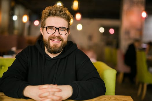 Close up portrait of young handsome freelance man wearing stylish eyeglasses on cafe. Happy confident student looking at camera, education and online work concept. Millennial generation and Gen Y