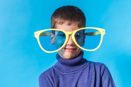 Cheerful little boy in big glasses express a surprised face isolated on blue background