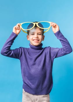 Cheerful little boy in big glasses express a surprised face isolated on blue background