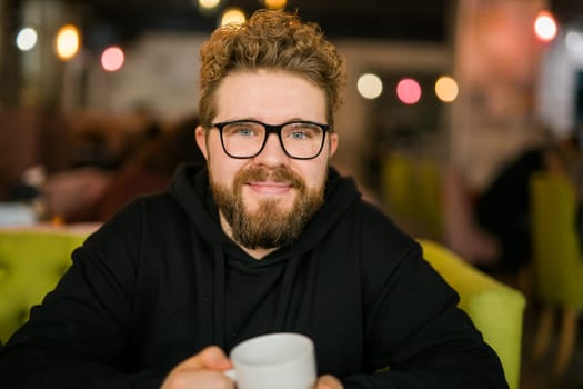 Bearded curly man smiling confident drinking coffee in restaurant or coffee shop. Millennial generation and Gen Y.