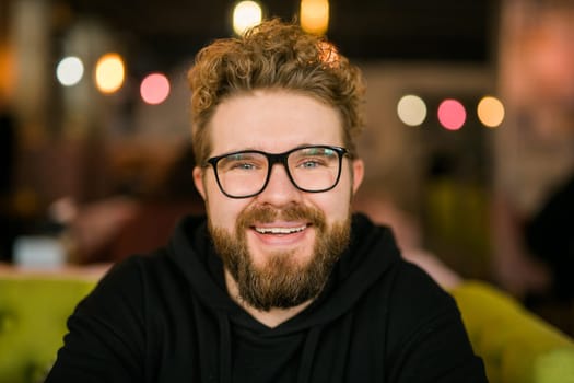 Close up portrait of young handsome freelance man wearing stylish eyeglasses on cafe. Happy confident student looking at camera, education and online work concept. Millennial generation and Gen Y