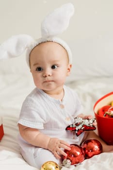 Christmas Baby in Santa Hat Child playing with baubles. Present Gift Box over Holiday Lights background and Merry Christmas