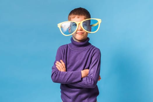 Cheerful little boy in big glasses express a surprised face isolated on blue background