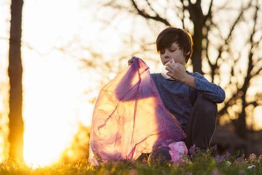 Cute teenage boy collects garbage in big pink bag in nature, in meadow on autumn evening at sunset. Environmental problems. We take care of nature. Saving planet. Proper parenting.
