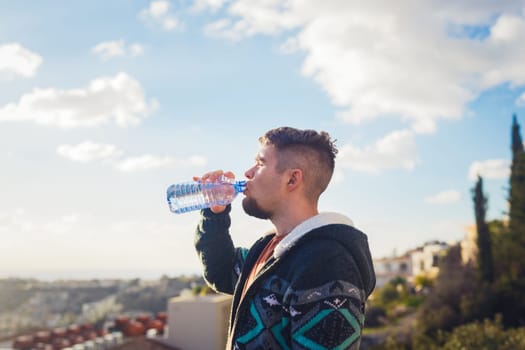 Man with beard drinking water from plastic bottle and enjoying view.