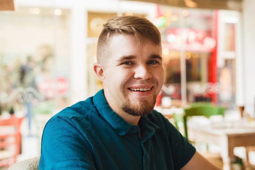 Close up of handsome Caucasian man with beard looking and smiling at camera with happy cheerful expression, sitting at restaurant, waiting for friends.