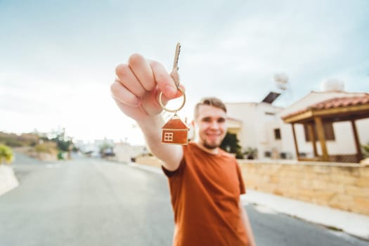 Joyful man shows keys on the background of new home.