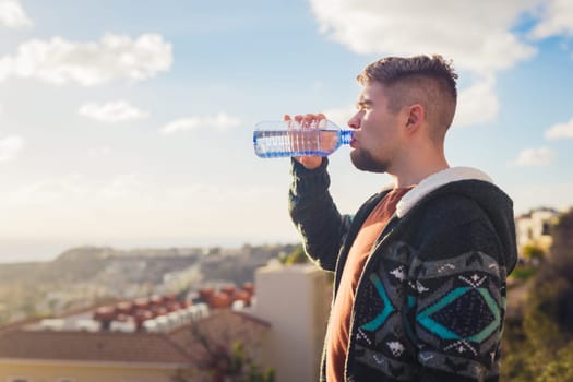 Man with beard drinking water from plastic bottle and enjoying view.