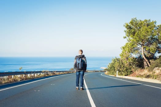 a man with a backpack walks alone on a mountain road