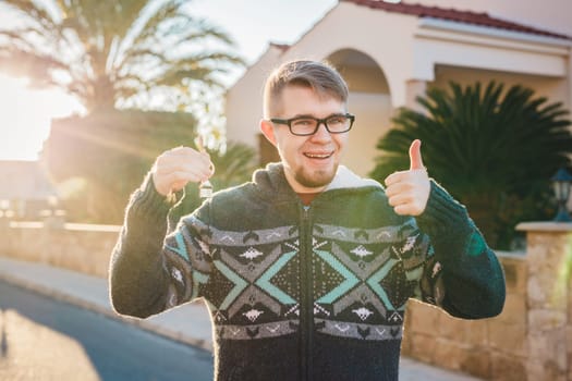 Portrait of a young happy man holding out new house key and gesturing thumbs up.