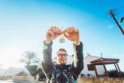 Joyful man shows keys on the background of new home.
