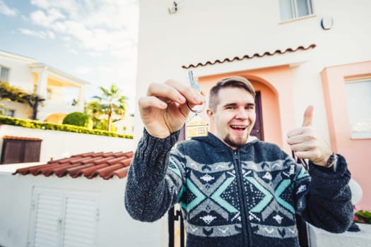 Portrait of a young man holding out new house key while gesturing thumbs up