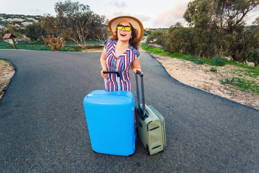 Travel, holiday, summer and vacation concept - Young woman is standing and laughing on road with suitcases.