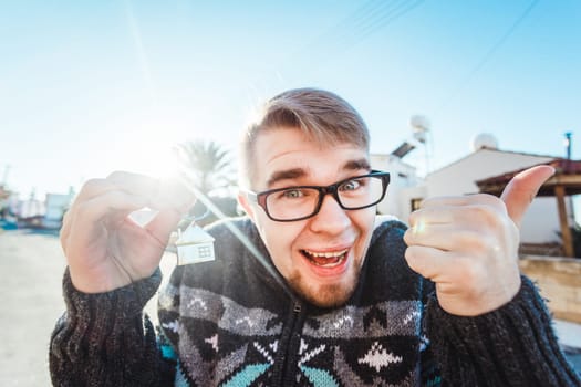 Portrait of a young man holding out new house key while gesturing thumbs up