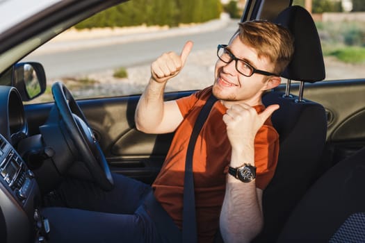 Young man smiling and showing thumbs up in his car.