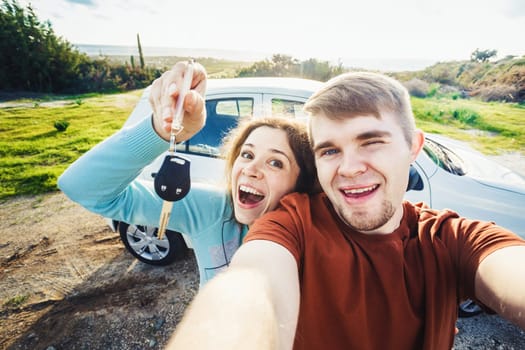 Young happy couple with keys to new car outdoor.