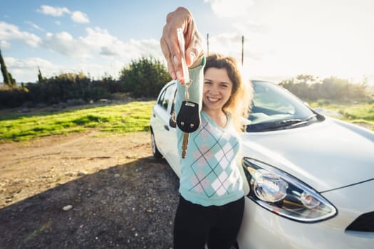 Young woman holding keys to new car and smiling at camera.