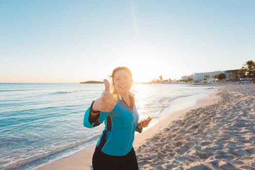 Successful female athlete doing positive thumbs up gesture and wearing earphones before running or exercising outdoor. Woman success in sport lifestyle
