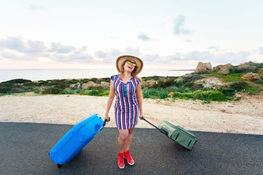 Travel, holiday, summer and vacation concept - Young woman is standing and laughing on road with suitcases.
